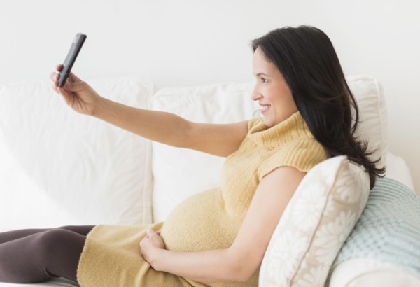 Pregnant Hispanic woman taking picture with cell phone