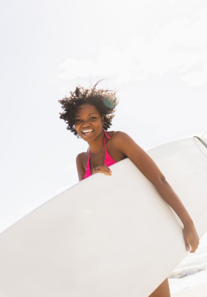 African American woman carrying surfboard on beach