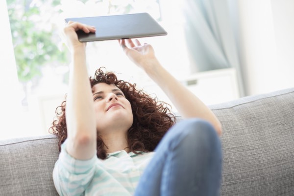 Hispanic woman using digital tablet on sofa