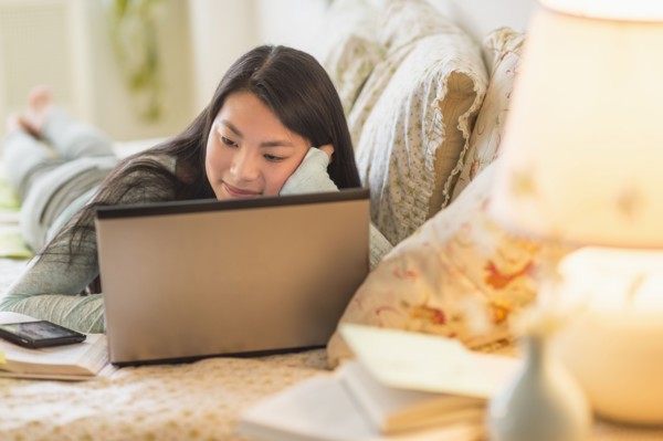 Mixed race teenage girl doing homework on bed