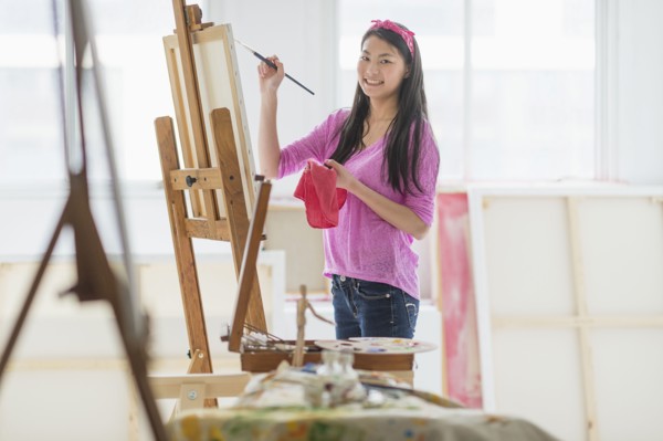 Mixed race teenage girl painting in studio