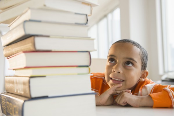 Mixed race boy looking up at stack of books