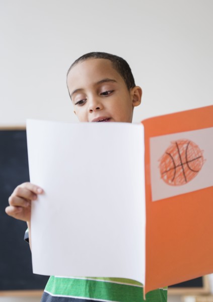 Mixed race boy reading report on basketball in class