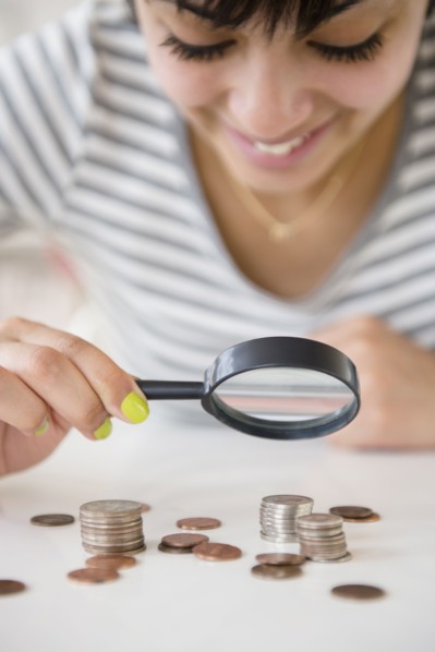 Mixed race woman examining stacks of coins with magnifying glass