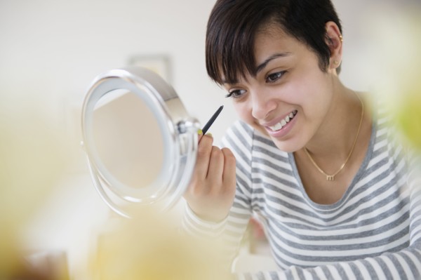 Mixed race woman applying makeup in mirror