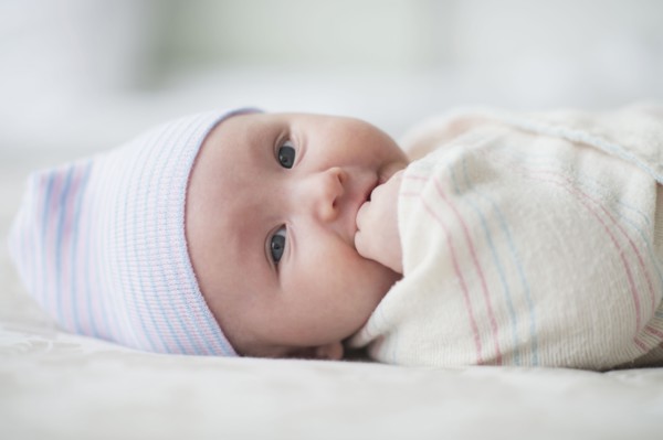 Swaddled Asian baby biting fingers on bed