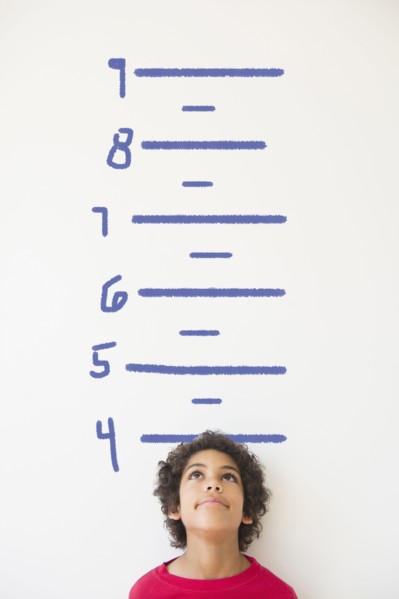 Mixed race boy measuring his height on wall chart