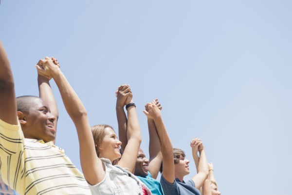 Low angle view of teenagers holding hands under blue sky