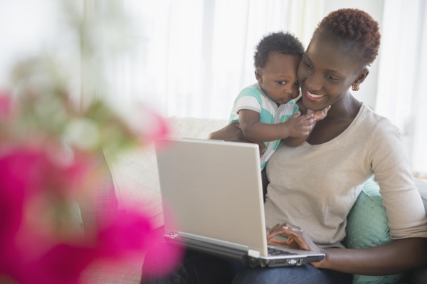 Black mother and son using laptop on sofa