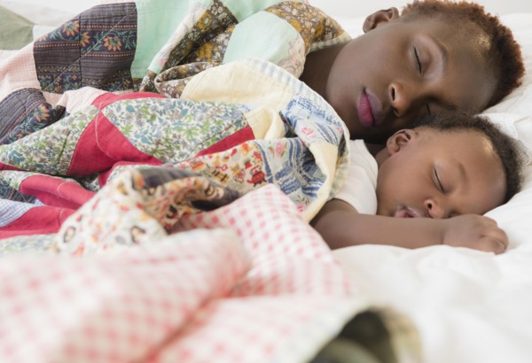 Black mother and son sleeping on bed