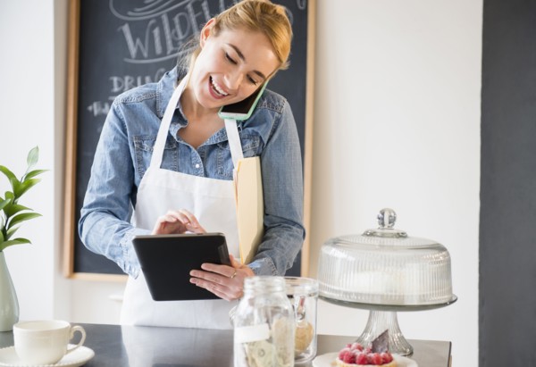 Caucasian barista using cell phone and digital tablet in cafe