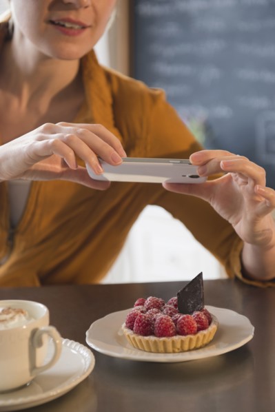 Caucasian woman taking cell phone photograph of dessert in cafe