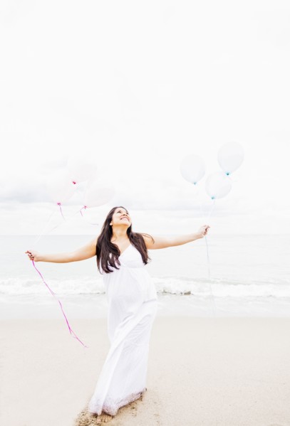 Pregnant mixed race woman holding balloons on beach