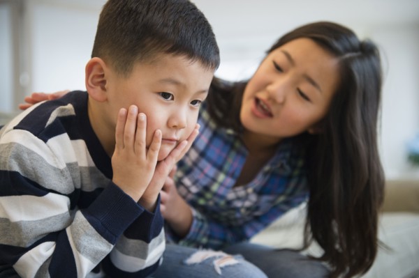 Asian sister comforting sad brother on sofa
