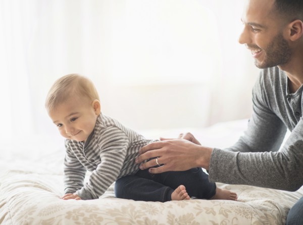 Father playing with baby son on bed
