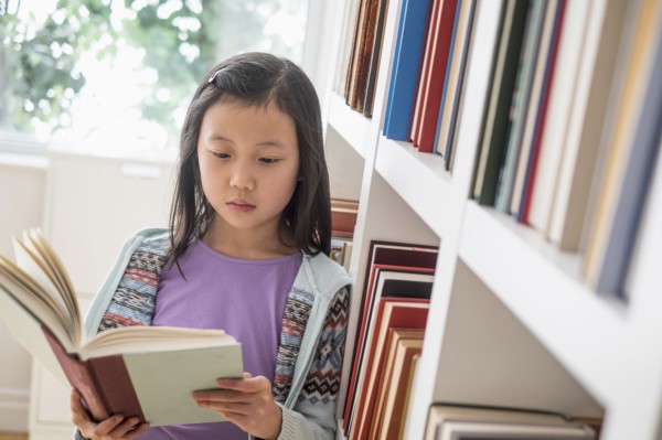 Chinese student reading book near library bookcase