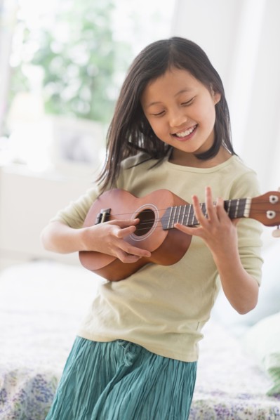 Chinese girl practicing ukulele in bedroom