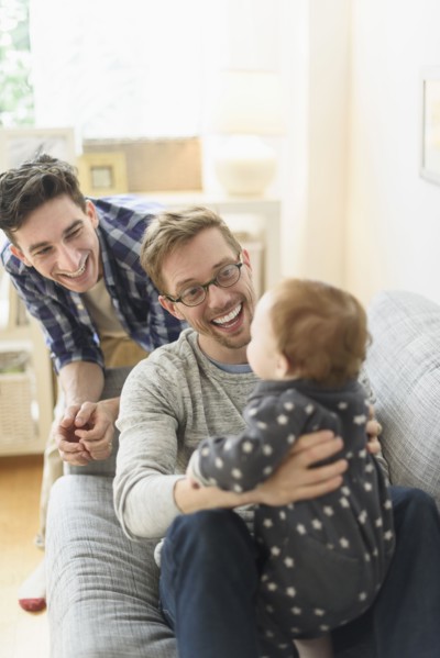 Caucasian gay fathers and baby relaxing on sofa
