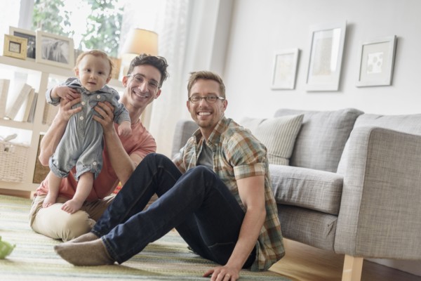 Caucasian gay fathers and baby playing in living room