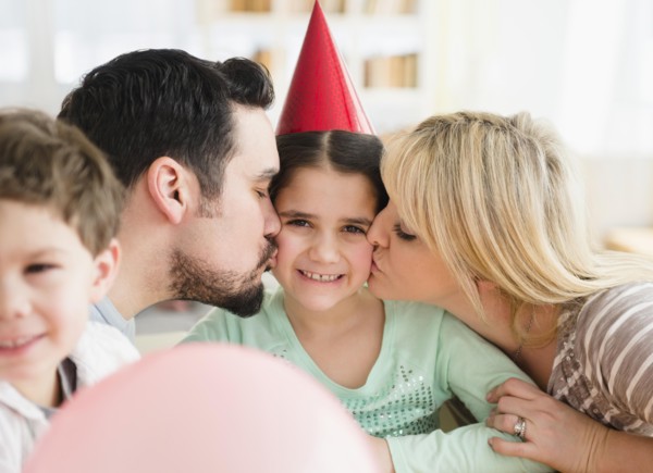 Caucasian parents kissing daughter at birthday party