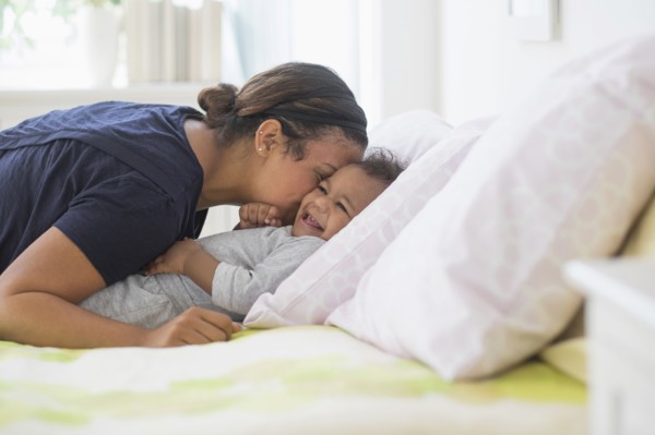 Mixed race mother kissing baby son on bed