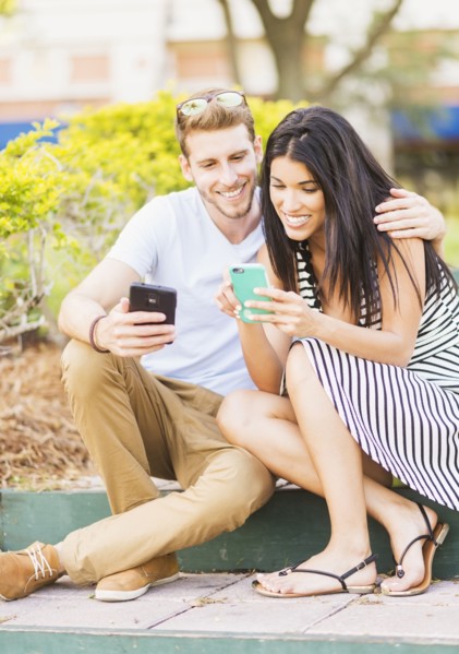 Hispanic couple using cell phones on sidewalk