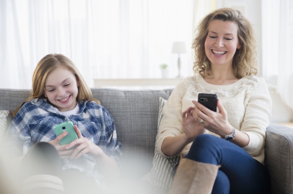 Caucasian mother and daughter using cell phones on sofa