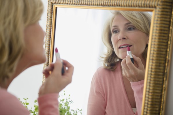 Caucasian woman applying lipstick in mirror