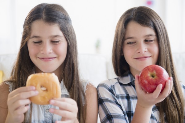 Caucasian twin sisters eating healthy and unhealthy snacks