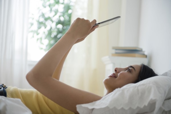 Hispanic woman using digital tablet in bed
