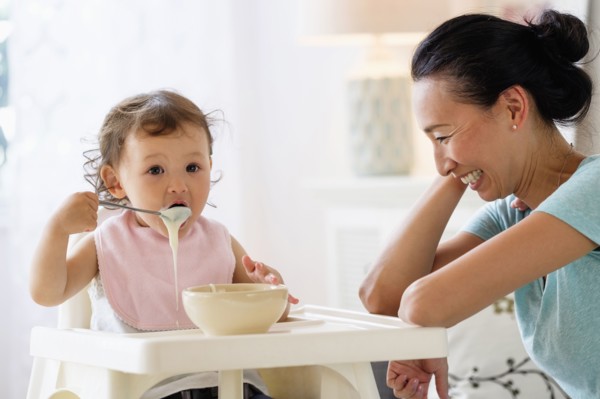 Mother watching baby daughter eat in high chair