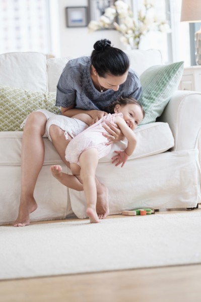 Mother playing with baby daughter on sofa