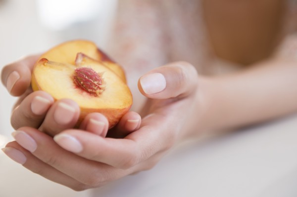 Hispanic woman holding halved peach