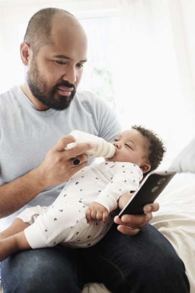 Father bottle feeding baby son and using cell phone