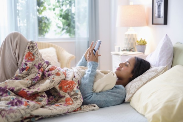 Mixed race woman using cell phone in bed