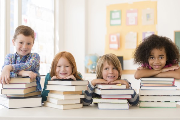 Students resting on stacks of books in classroom