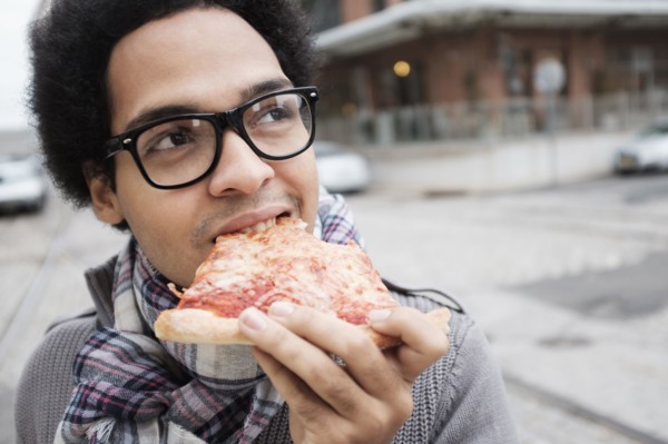 Mixed race man eating pizza outdoors