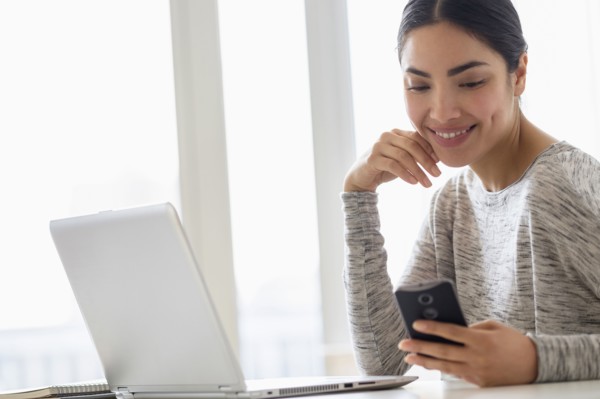 Hispanic woman using cell phone and laptop