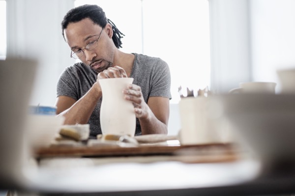 Black artist shaping ceramic vase in studio