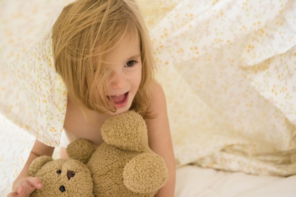 Caucasian girl playing with teddy bear under blankets