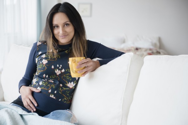 Pregnant Caucasian woman drinking cup of coffee on sofa