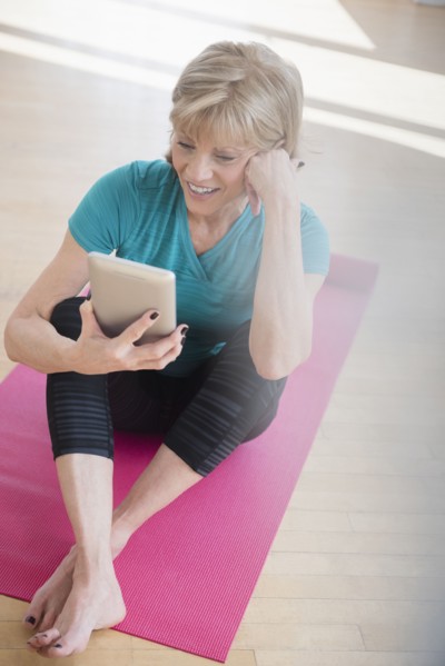 Older Caucasian woman on exercise mat using digital tablet