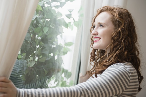 Caucasian woman opening curtains at window