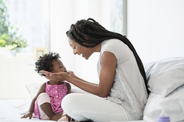 Black woman cupping face of baby daughter on bed