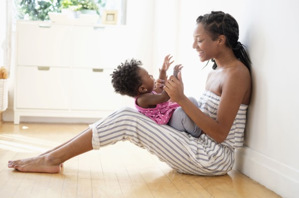 Black woman sitting on floor clapping hands with baby daughter