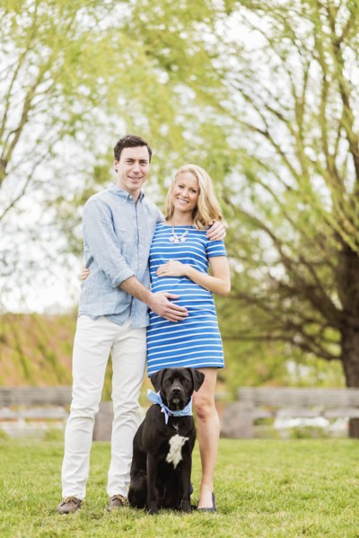 Smiling Caucasian man and expectant mother posing with dog in park