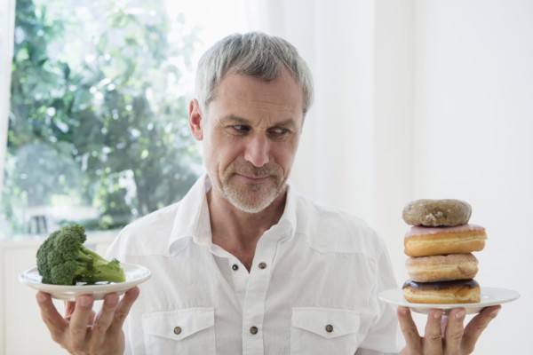 Older Caucasian man choosing between broccoli and donuts