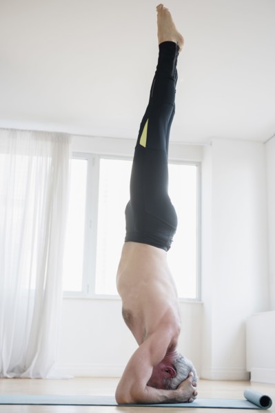 Older Caucasian man doing headstand on exercise mat