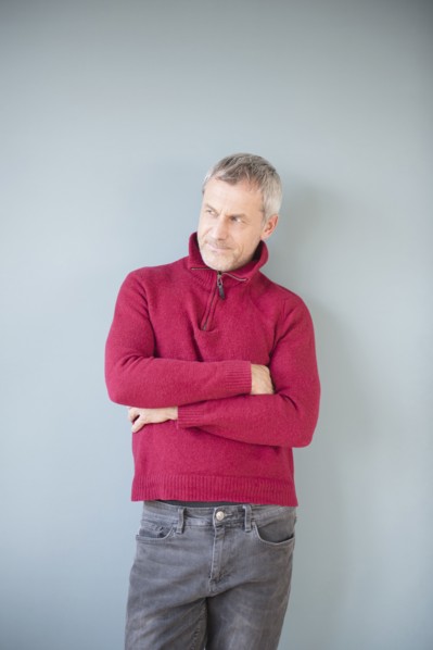 Older Caucasian man wearing sweater leaning on wall