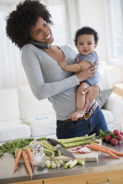 Mother talking on telephone while holding baby son in kitchen